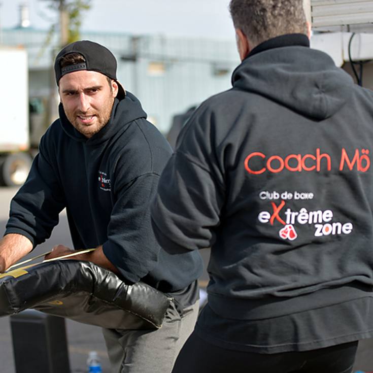Coach Alex tient un bouclier de frappe pendant que Coach Mö l'observe